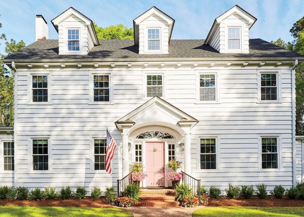 white colonial home with pink front door and american flag waving, featured in southern living