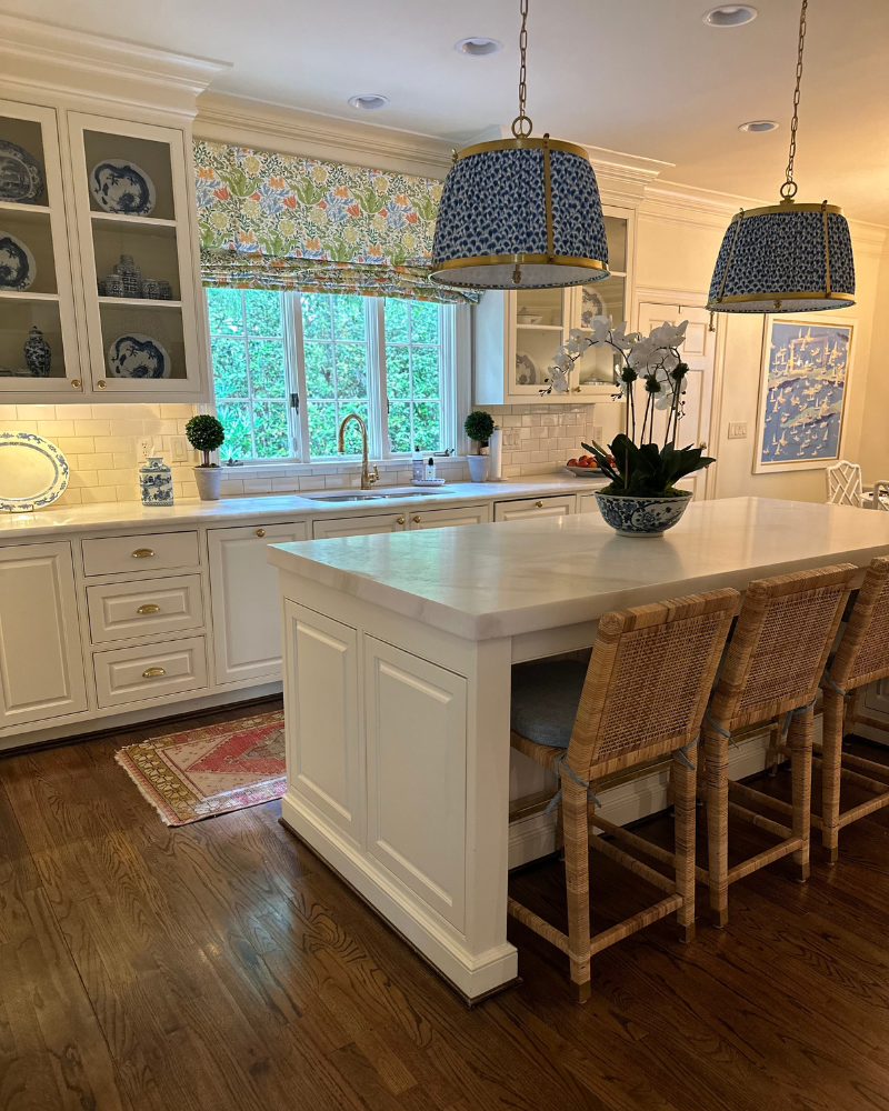 classic all-white kitchen with blue drum shades, a floral roman shade, chinoiserie china