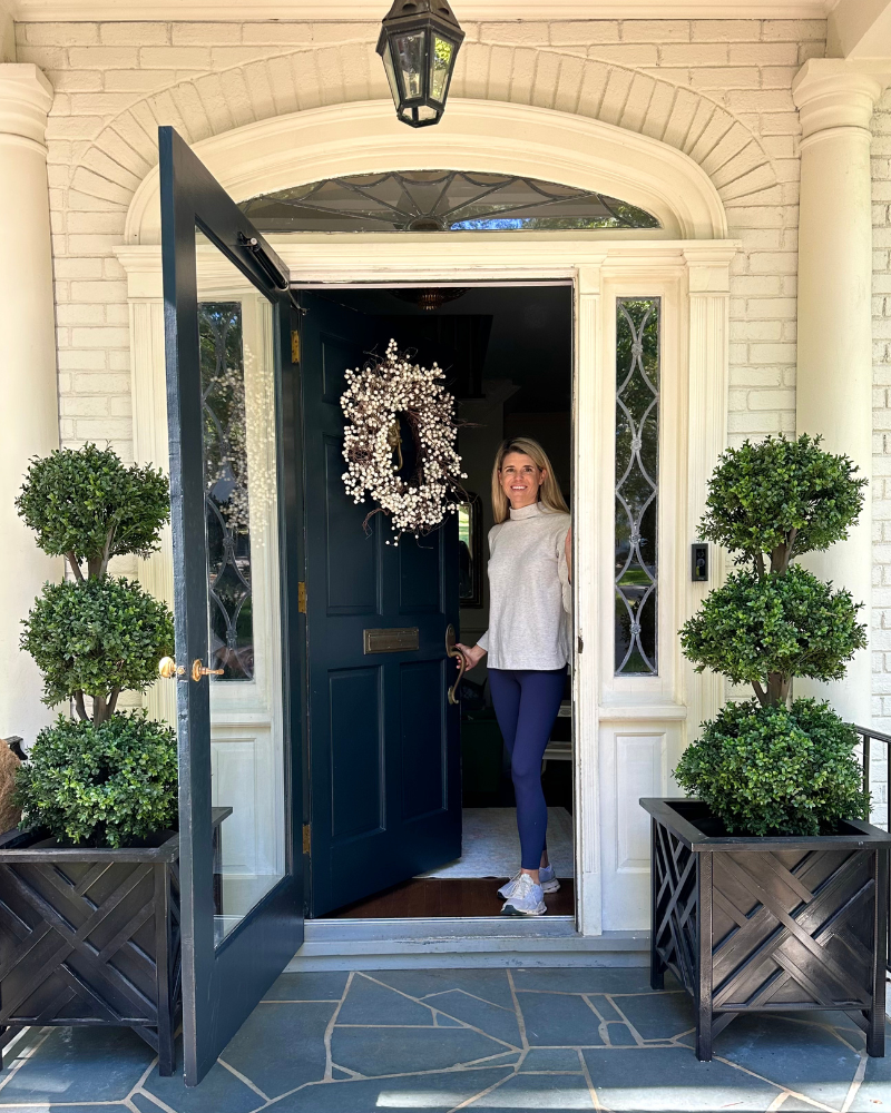 Crystal Moore, founder of Garden & Grace, opening her front door thats flanked by amazon topiaries
